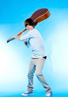 a young man is holding a guitar and posing for a photo in front of a blue background