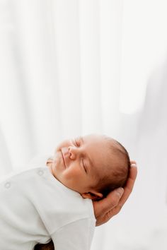 a baby is being held up to the camera by its mother's hand in front of a white curtain