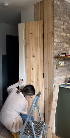 a woman sitting on a stepladder in front of a brick wall and wooden paneling