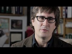 a man with glasses is looking at the camera in front of a bookshelf