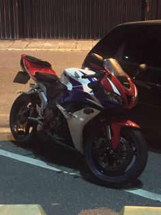 a red, white and blue motorcycle parked next to a black car in a parking lot