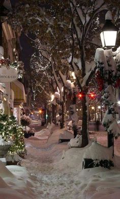 a snowy city street at night with christmas decorations on the trees and lights in the snow