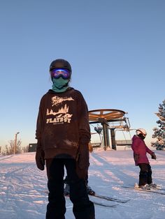 two people standing in the snow with skis on and one person wearing goggles