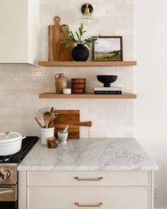 a white kitchen with marble counter tops and wooden shelves above the stove, along with pots and pans