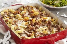 a red casserole dish filled with pasta and meat, next to a salad