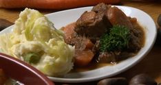 a white plate topped with meat and mashed potatoes next to carrots on a table