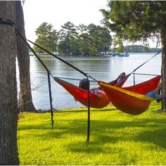 two people sitting in hammocks on the grass next to a body of water