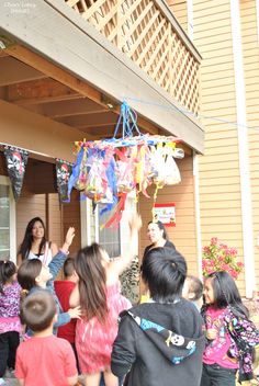 a group of people standing around each other in front of a house with kites hanging from the roof