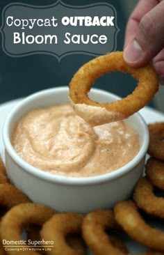 a person dipping some onion rings into a small white bowl filled with mayonnaise