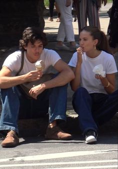 two people sitting on the ground eating ice cream