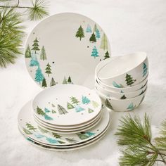 a stack of white and green christmas plates with trees on them, surrounded by pine branches