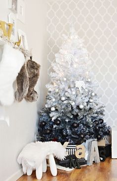 a small christmas tree in the corner of a room with white and silver decorations on it