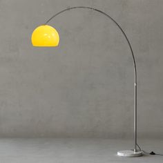 a floor lamp with a yellow shade on the base and a grey wall behind it