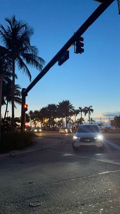 a car is driving down the street at night time with palm trees in the background