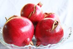 four pomegranates in a glass bowl on a white background