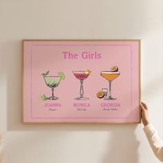 a woman holding up a framed poster with different cocktails on it's side