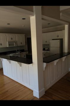 an empty kitchen with white cabinets and black counter tops in the middle of a wood floored room