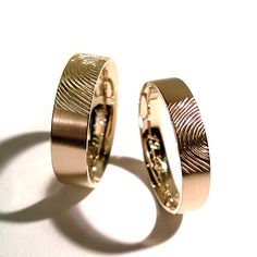 two gold wedding rings sitting next to each other on a white surface with shadows from them