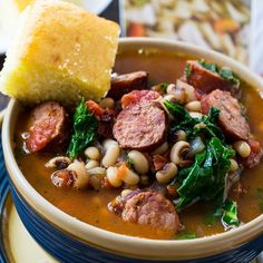 a bowl of soup with sausage, beans and spinach on a plate next to a piece of bread