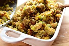 a casserole dish filled with stuffing next to a skillet on a wooden table