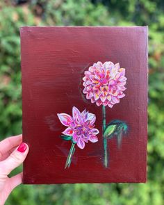 a painting of two flowers painted on a piece of wood with green trees in the background