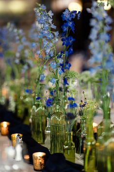 many vases with flowers in them are lined up on a long table, along with candles