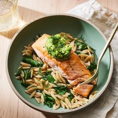 a bowl filled with pasta and broccoli on top of a wooden table next to a glass of water