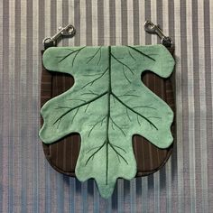 a green leaf shaped purse sitting on top of a striped tablecloth covered floor next to a metal hook