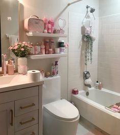 a white bathroom with pink accessories on the shelves above the toilet and bathtub area