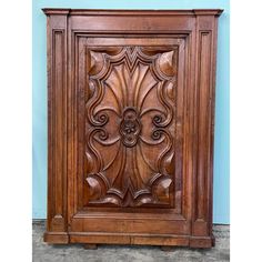 an ornate wooden cabinet with carvings on the front and sides, against a blue wall