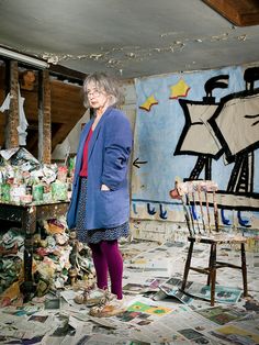 an older woman standing in the middle of a room full of paper and magazines on the floor