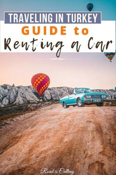 a car driving down a dirt road with hot air balloons in the sky