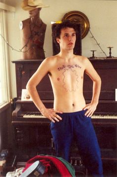 a shirtless man standing in front of a piano with his hands on his hips