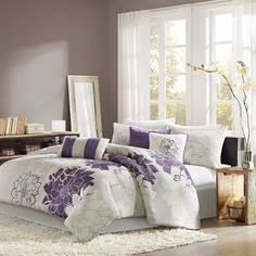 a bed with purple and white comforters in a room next to a window,