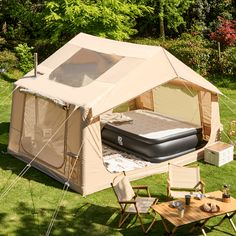 a tent set up in the grass with an air mattress and table next to it