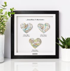 two heart shaped paper cut maps in a black frame next to a potted plant