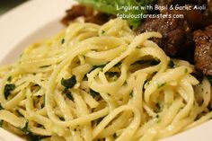 a white plate topped with pasta and meat next to greens on top of a table