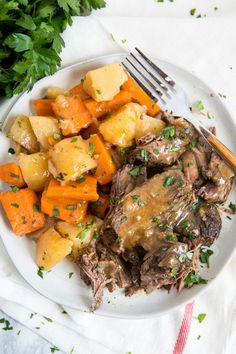 a white plate topped with meat, potatoes and carrots next to green parsley