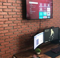 two computer monitors sitting on top of a wooden desk in front of a brick wall