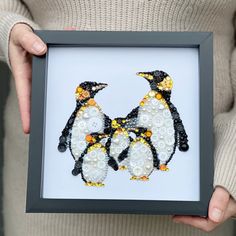 a person holding a framed picture with two penguins made out of buttons and beads on it