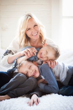 a woman and two children laying on top of a white bed with their arms around each other