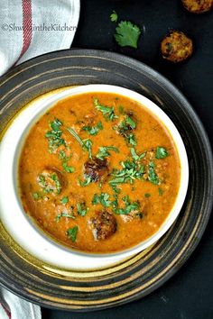 a bowl of soup with meatballs and cilantro on the side next to some bread