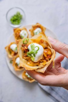 a hand holding up a small tortilla with meat and sour cream on top