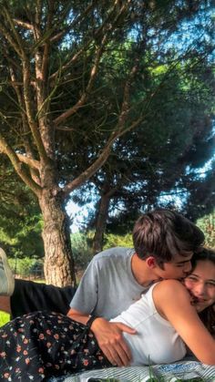 a man and woman cuddle under a tree in the shade on a picnic blanket