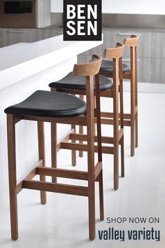 four bar stools with black leather seats are on the counter in front of an open kitchen