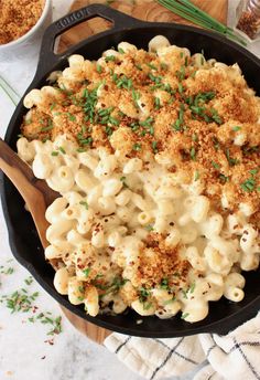 a skillet filled with macaroni and cheese on top of a wooden cutting board