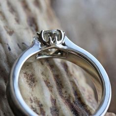 a silver ring sitting on top of a piece of wood next to a stone wall