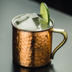 a close up of a metal cup with ice and a lime on the rim, sitting on a table