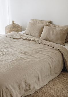 a bed with beige linens and pillows in a white room next to a wicker basket