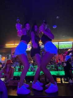 two young women standing on top of a bar in front of a neon green light